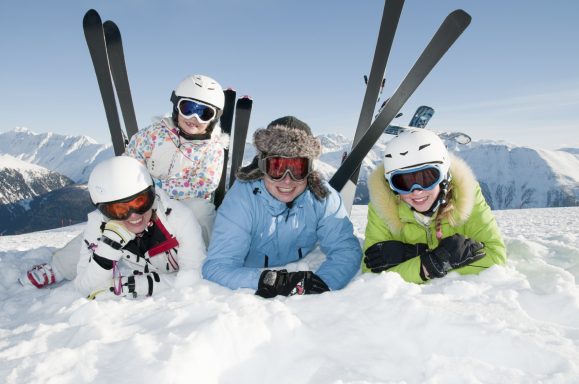 Quatre skieurs posent dans la neige avec des montagnes en arrière-plan.