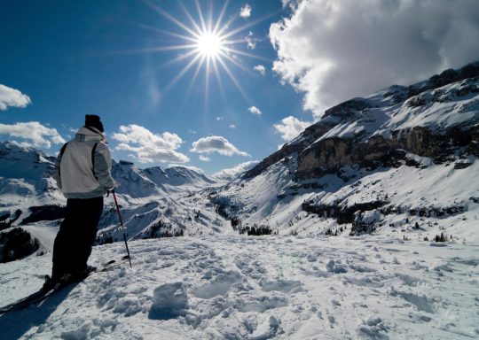 Skieur sur un paysage alpin enneigé sous un ciel ensoleillé.