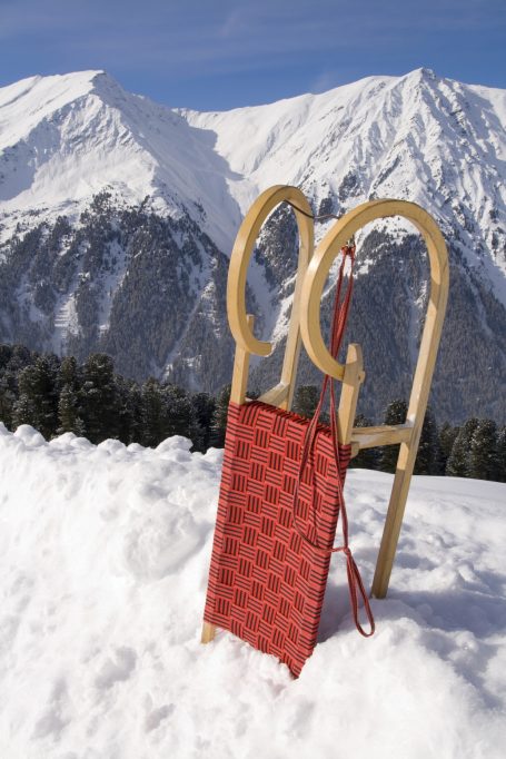 Luge en bois avec un traîneau rouge, devant des montagnes enneigées.