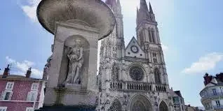 Église avec statue en premier plan, ciel ensoleillé et architecture détaillée.