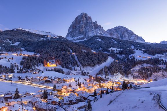 Vue panoramique d'un village alpin enneigé avec des montagnes à l'arrière-plan.