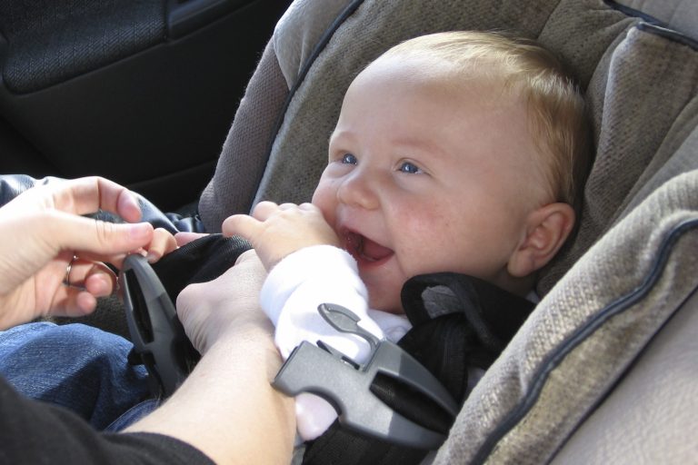 Bébé souriant dans un siège auto, les mains occupées à jouer.