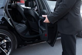 Une personne en costume ouvre la porte arrière d'une voiture noire.