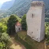 Ruine d'une tour en pierre entourée de végétation et de montagnes.