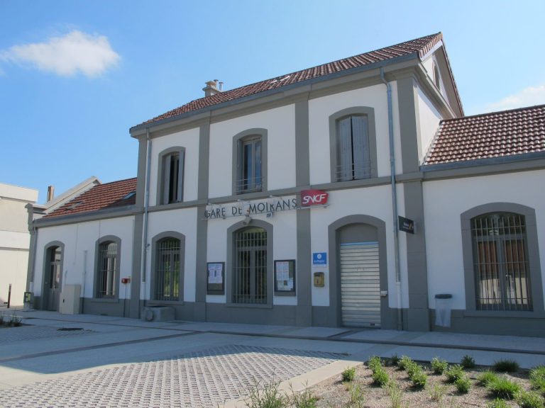 Bâtiment en pierre avec des fenêtres et une porte, devant une zone pavée.