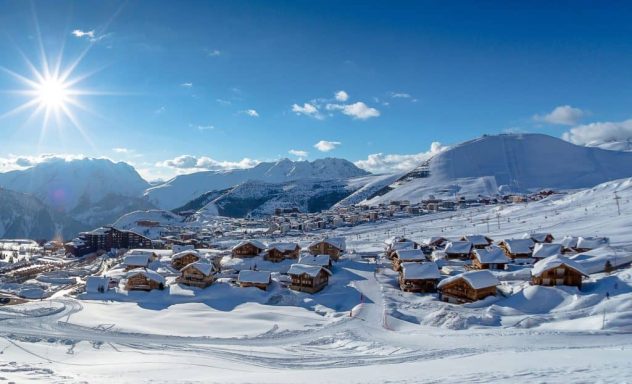 Paysage enneigé avec des chalets, montagnes en arrière-plan et ciel bleu lumineux.