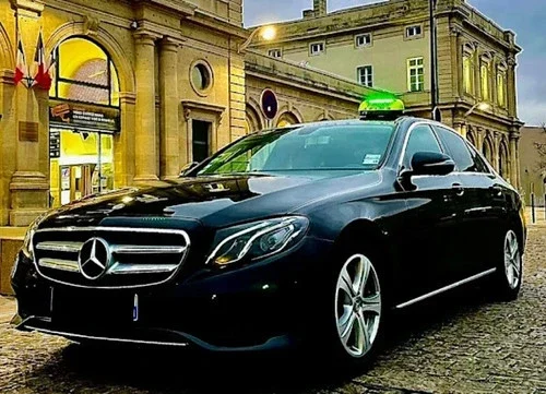 taxi ViP Voiron, Voreppe, Tullins, Moirans; Isère Taxi noir Mercedes-Benz E-Class devant un bâtiment sous un ciel crépusculaire.