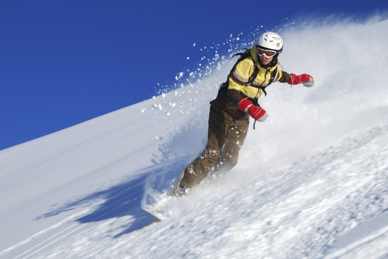 Un skieur lançant de la poudreuse sur une pente enneigée sous un ciel bleu.