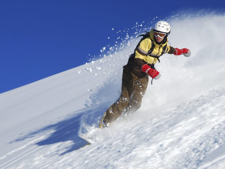 Skieur descendant une pente enneigée sous un ciel bleu.