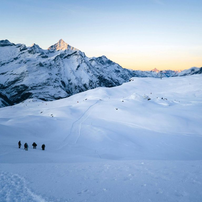 Groupe d'alpinistes marchant sur un paysage montagneux enneigé au coucher du soleil.