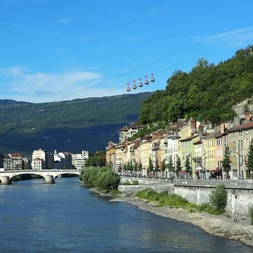 Rivière avec bâtiments colorés en longueur, téléphérique surplombant la colline verdoyante.