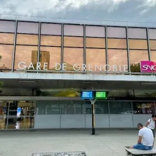 Façade moderne de la gare de Grenoble avec des reflets et des panneaux d'information.