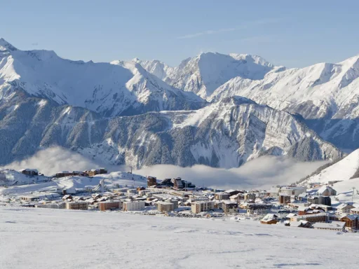 Vue panoramique d'un village enneigé entouré de montagnes majestueuses.