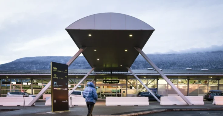 Entrée moderne d'un aéroport avec toit en forme de soucoupe et paysage montagneux en arrière-plan.