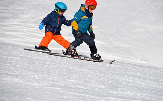 Deux enfants skiant sur une pente enneigée, l'un aidant l'autre.